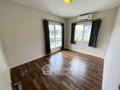 Spacious empty room with hardwood floors and large windows in modern apartment.