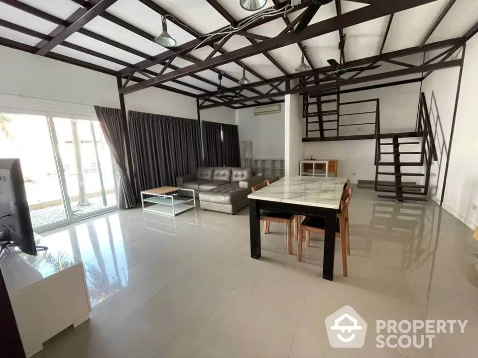 Spacious living room with high ceilings, exposed beams, and glossy tiled floors, featuring large windows for ample natural light.