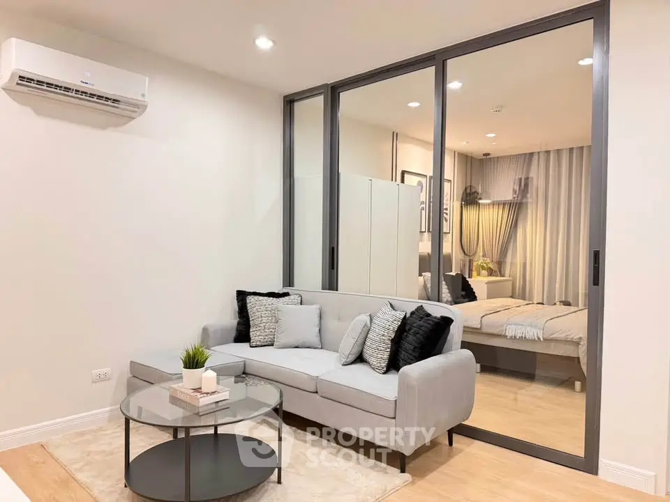 Modern living room with stylish decor and glass partition leading to bedroom, featuring cozy sofa and chic accents.