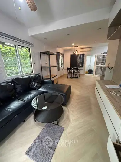 Modern living room with black leather sofa and open dining area, featuring sleek design and natural light.