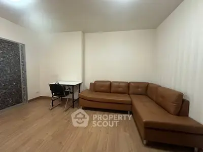Spacious living room with modern brown leather sectional sofa and sleek wooden flooring.