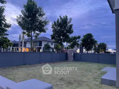 Spacious backyard with lush lawn and modern fence in suburban neighborhood at dusk.