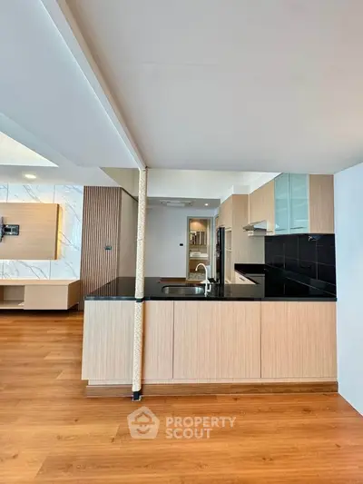 Modern open-layout kitchen with sleek black countertops and wooden flooring, perfect for contemporary living.