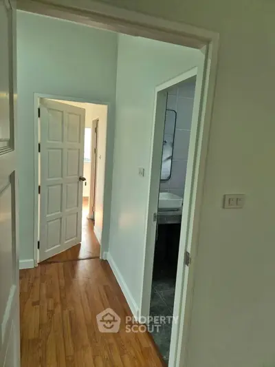 Bright hallway with wooden flooring leading to multiple rooms in a modern home.