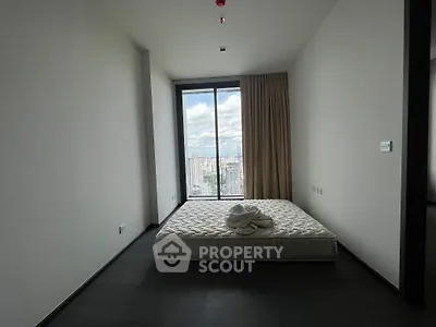 Spacious bedroom with large window offering stunning city view, featuring minimalist decor and natural light.
