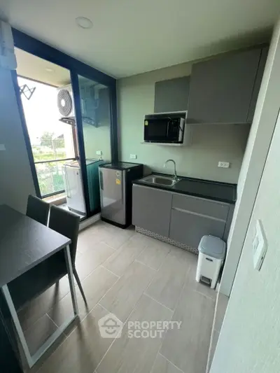 Modern compact kitchen with sleek cabinets and appliances, featuring a small dining area and balcony view.