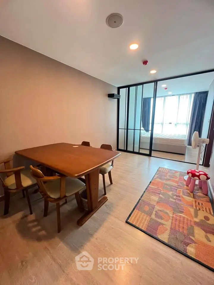 Spacious modern dining area with wooden table and chairs, adjacent to a cozy bedroom with sliding glass doors.