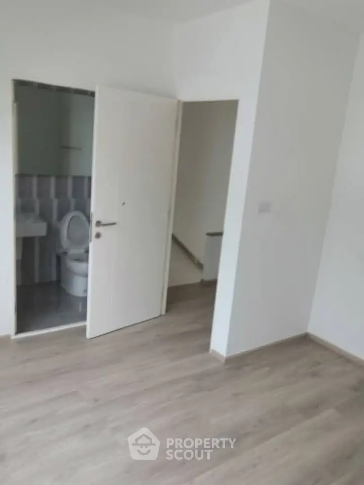 Spacious room with wooden flooring and attached bathroom in modern apartment.