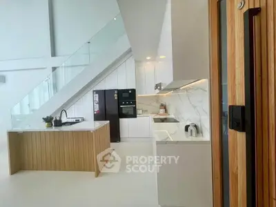 Modern kitchen with sleek design, featuring an island and built-in appliances under a stylish staircase.