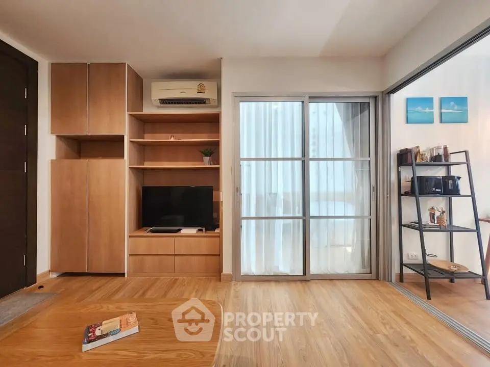 Modern living room with wooden flooring and sliding glass doors leading to a balcony.