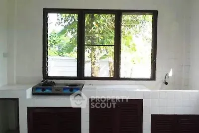 Bright kitchen with large window and gas stove, offering a view of lush greenery.