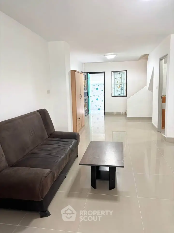 Spacious living room with modern sofa and sleek coffee table in a bright, tiled interior.