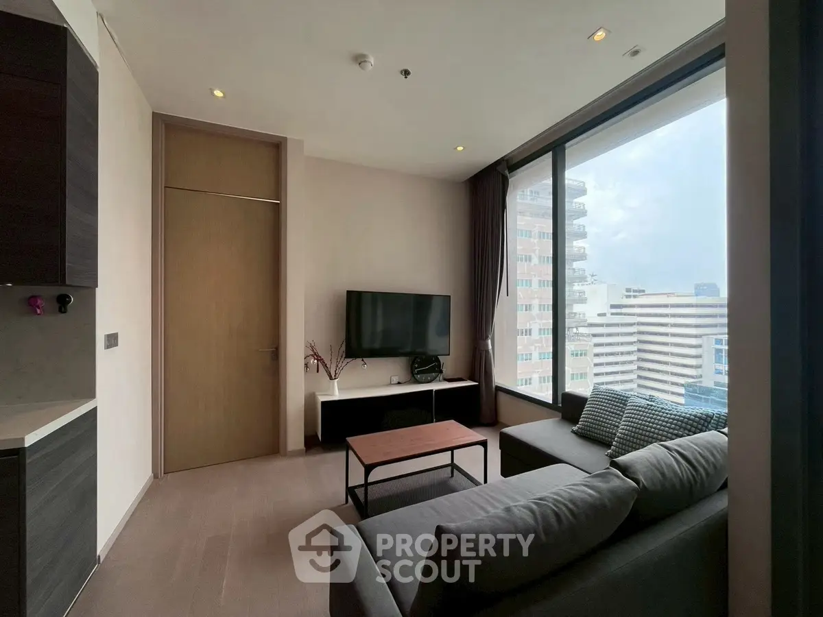 Modern living room with large window and city view, featuring sleek furniture and a wall-mounted TV.