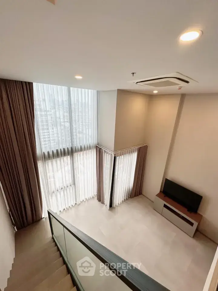 Modern duplex living room with high ceilings and large windows offering city views.