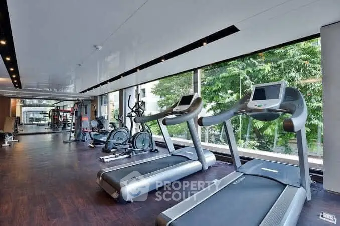 Spacious modern gym with large windows and state-of-the-art equipment in luxury building.