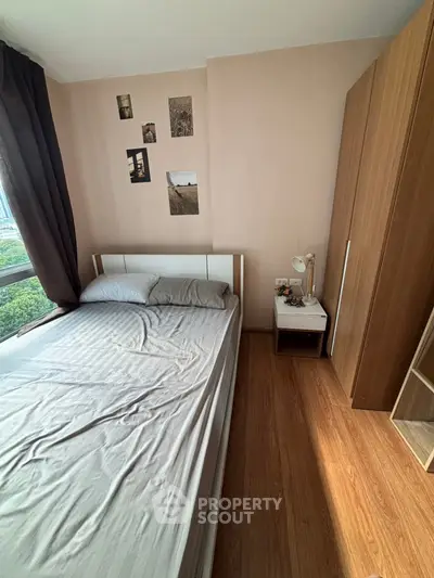 Cozy bedroom with wooden flooring and large window offering natural light.