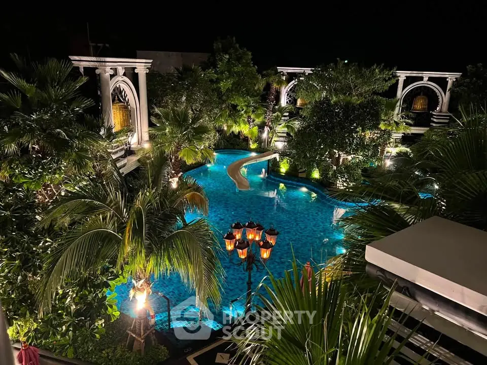 Luxurious nighttime pool view surrounded by lush greenery and elegant architecture, perfect for relaxation.