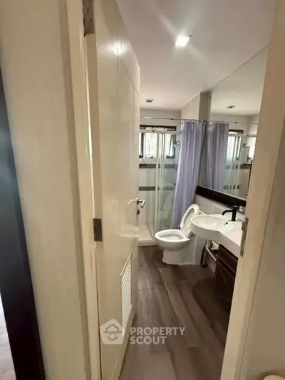 Modern bathroom with sleek fixtures and wood flooring, featuring a shower and vanity.