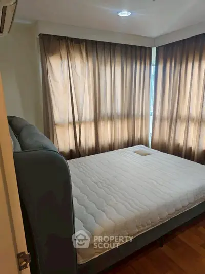 Cozy bedroom with large windows and elegant curtains, featuring a comfortable bed and wooden flooring.