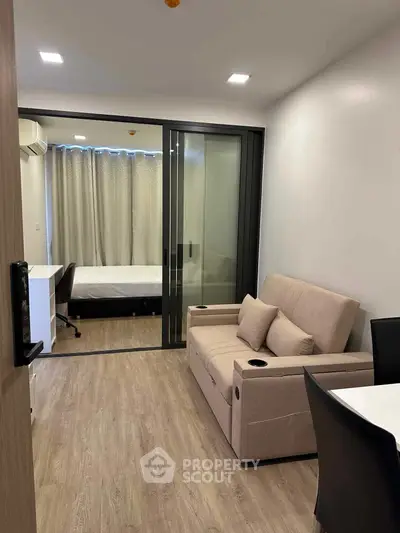 Modern apartment interior with sliding glass doors separating living room and bedroom, featuring sleek furniture.