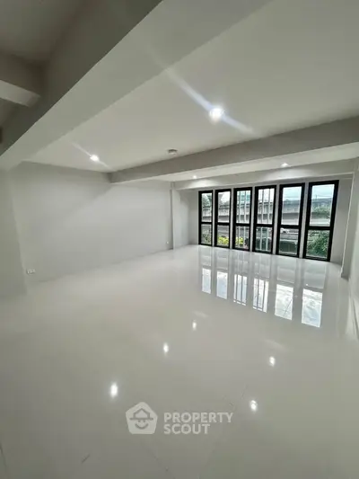 Spacious modern living room with large windows and glossy white flooring, offering abundant natural light.