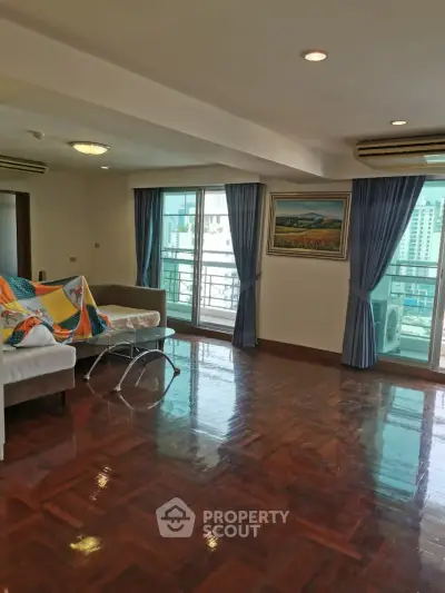 Spacious living room with polished wooden floors and large windows offering city views.