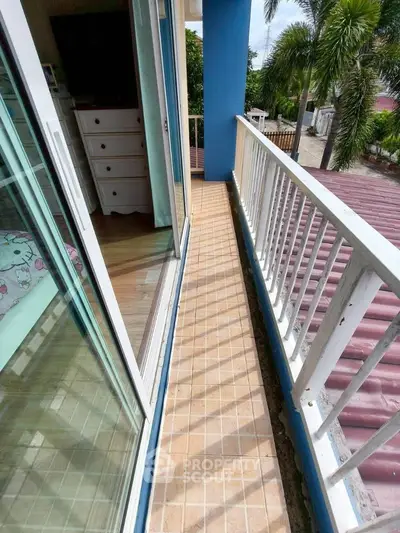 Charming narrow balcony with tiled flooring and white railing, overlooking lush greenery and neighborhood view.