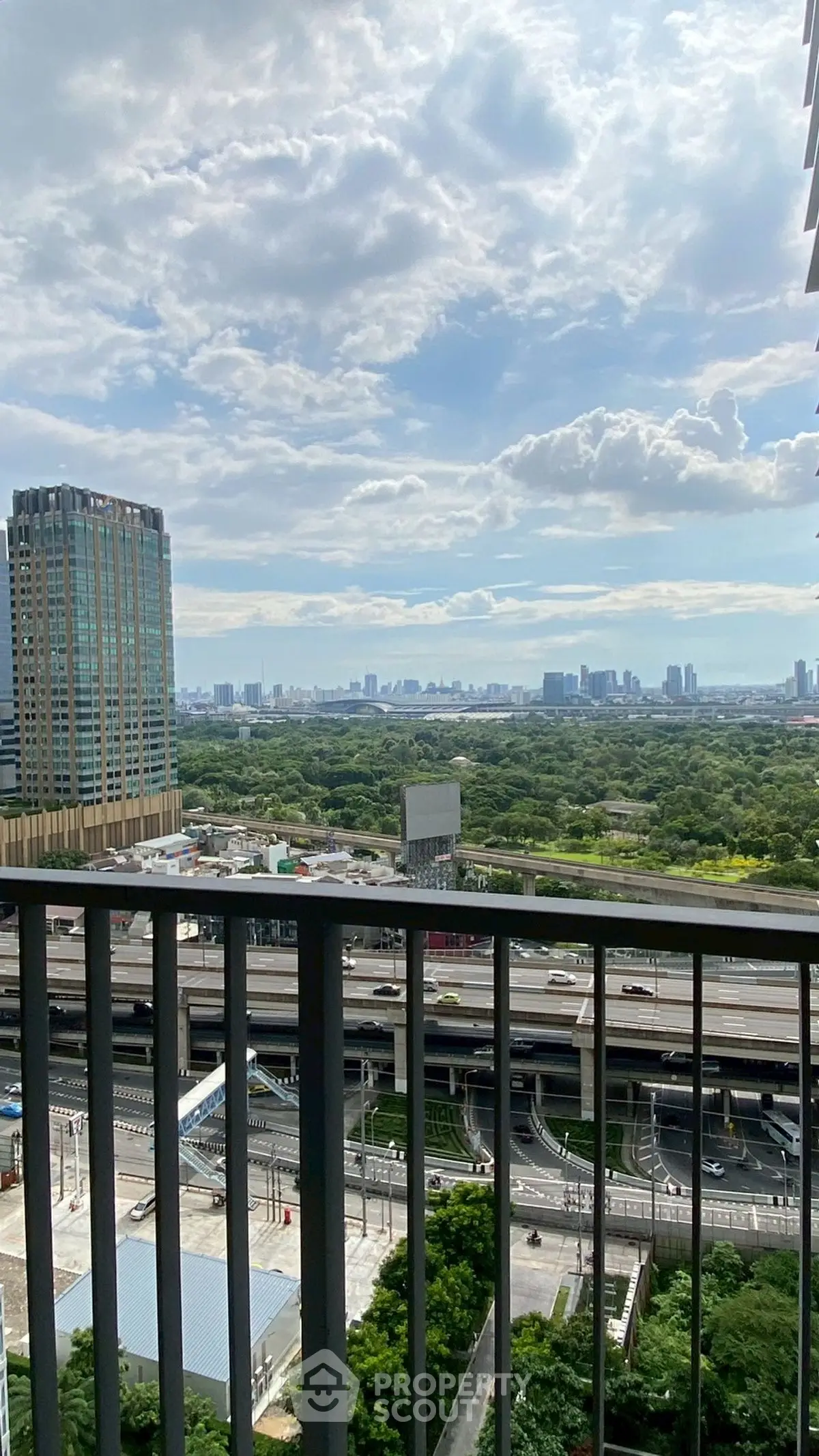 Stunning cityscape view from high-rise balcony overlooking lush greenery and urban skyline.