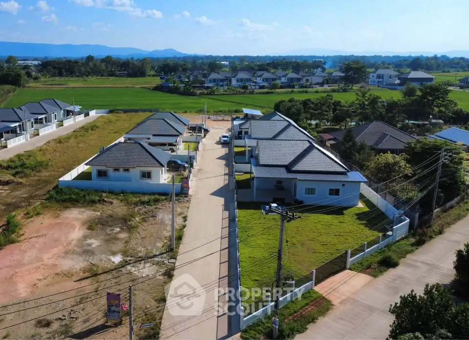 Aerial view of modern suburban homes with lush green surroundings and clear blue skies.