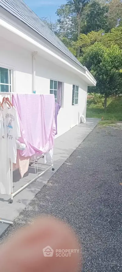Charming exterior view of a white house with laundry area and lush greenery.