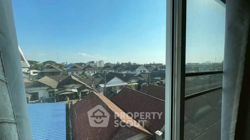 Stunning urban view from a window showcasing a vibrant neighborhood with diverse rooftops under a clear blue sky.