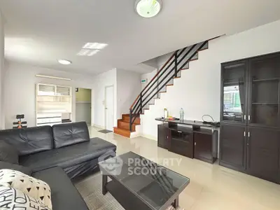 Spacious modern living room with sleek black furniture and elegant staircase in a bright, airy home.