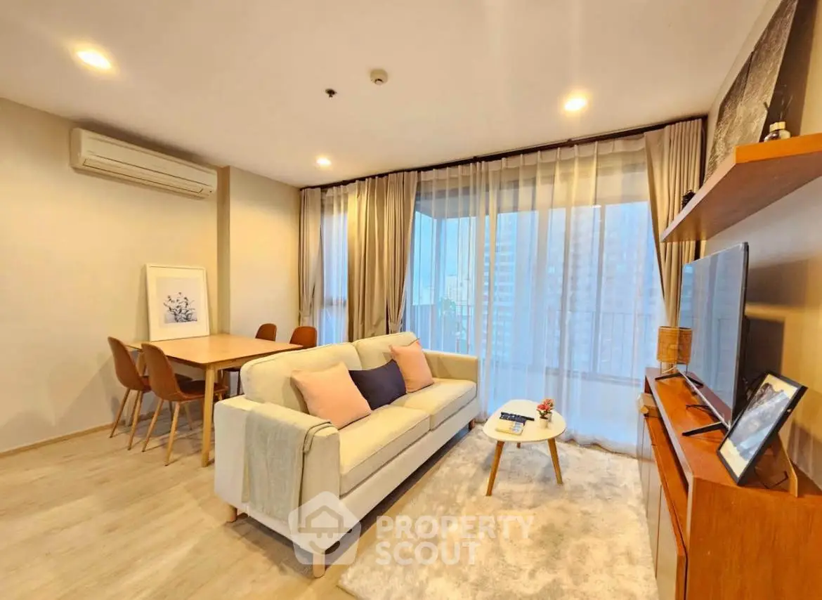 Modern living room with cozy sofa, dining area, and large windows offering city view.