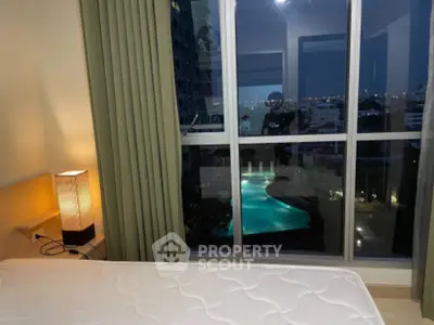 Cozy bedroom with stunning night view of illuminated pool and cityscape.