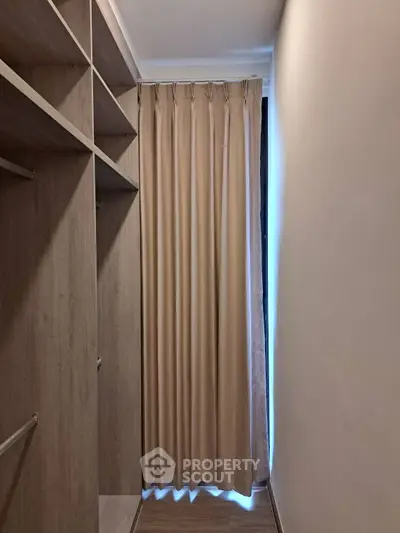 Spacious walk-in closet with elegant wooden shelving and soft beige curtains.