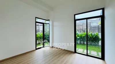 Spacious room with large windows overlooking a lush garden, featuring elegant wooden flooring.