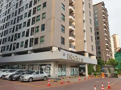 Modern apartment building exterior with parking area and retail shops at the base.
