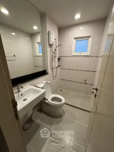 Modern bathroom with sleek fixtures and neutral tiles, featuring a shower and toilet.