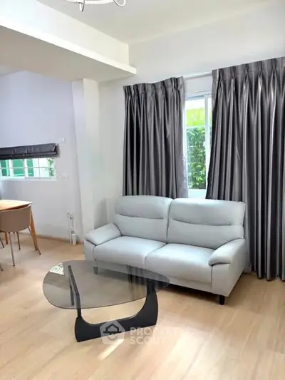 Modern living room with stylish gray sofa and glass coffee table, featuring elegant curtains and natural light.