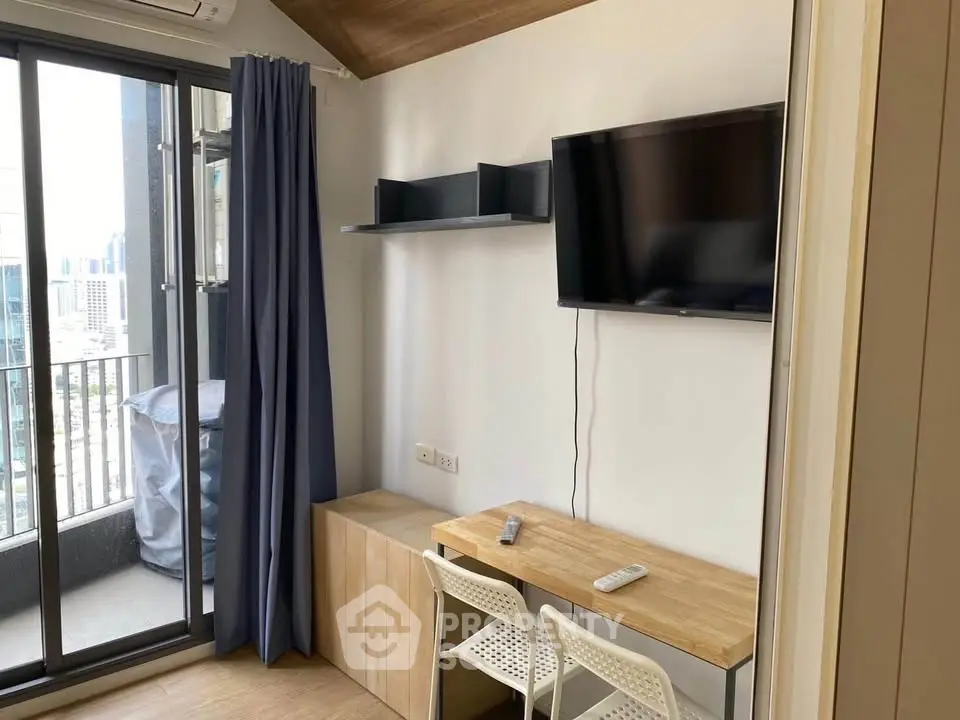 Modern apartment with balcony, wall-mounted TV, and stylish workspace in urban setting.