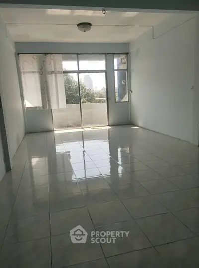 Spacious living room with large windows and tiled flooring, offering natural light and city views.