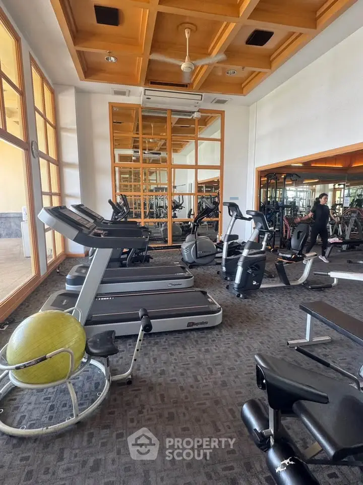 Spacious gym with modern equipment and mirrored walls in luxury building.