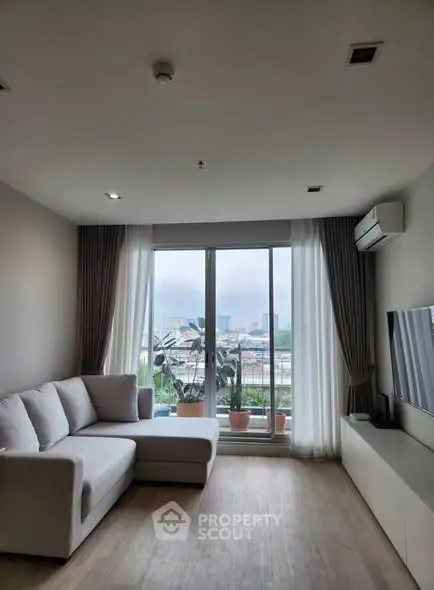 Modern living room with large window and city view, featuring a cozy sofa and sleek TV setup.