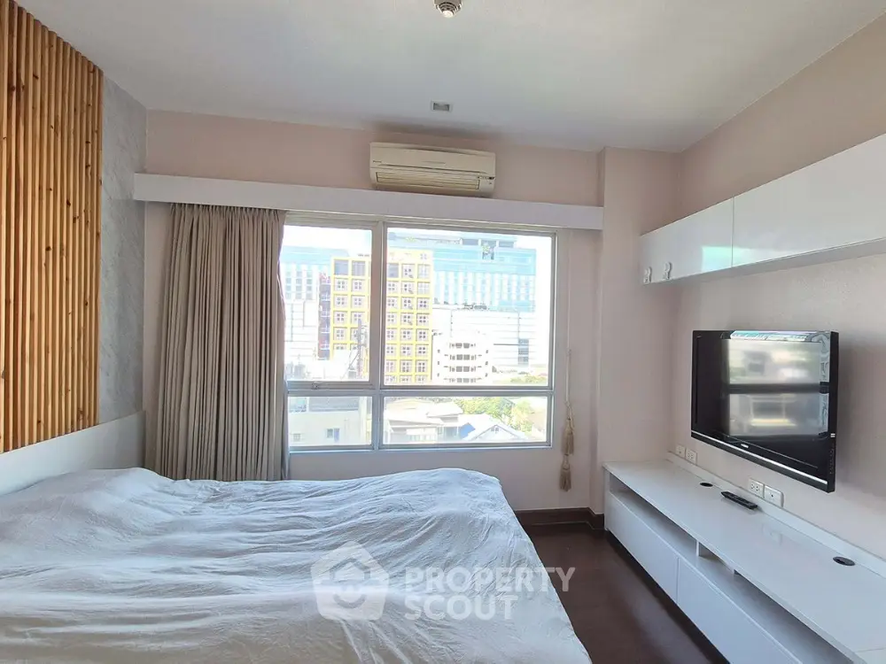 Modern bedroom with large window and city view, featuring sleek white furniture and air conditioning.