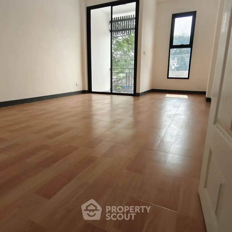 Spacious empty room with wooden flooring and large windows offering natural light.