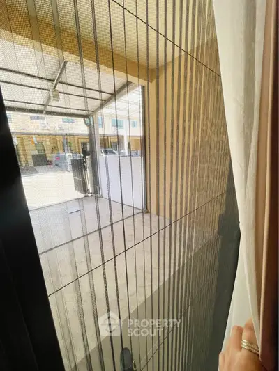 Modern patio view through glass door with elegant curtain and outdoor seating area.