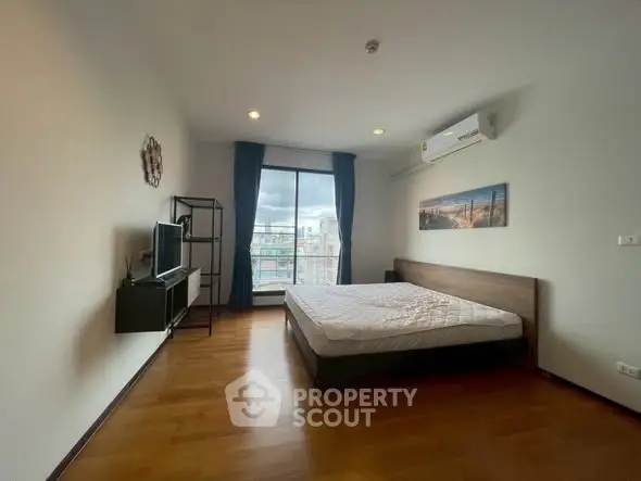 Spacious bedroom with large window and city view, featuring modern furnishings and wooden flooring.