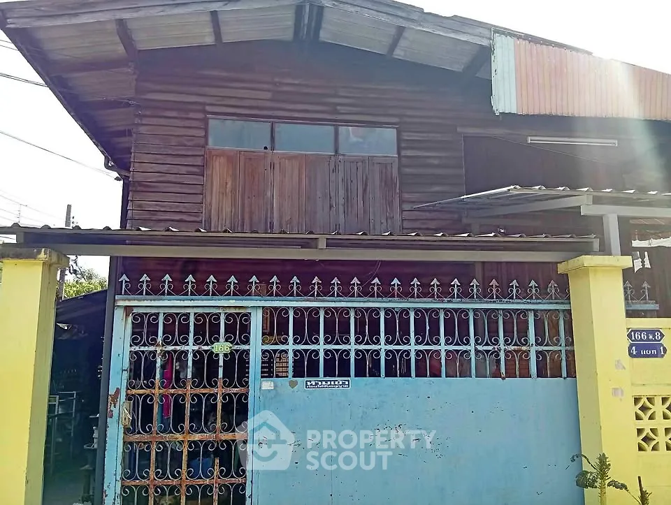 Charming rustic wooden house with metal gate and corrugated roof, perfect for renovation enthusiasts.