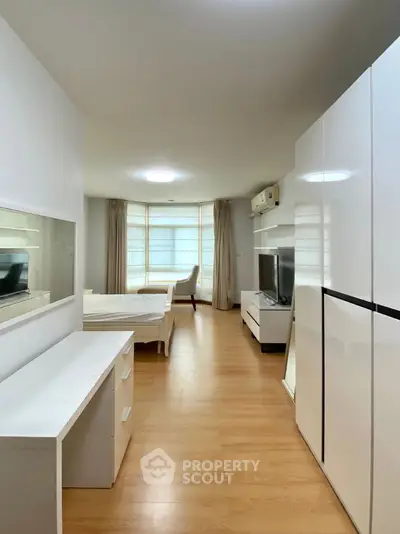 Spacious modern bedroom with wooden flooring and sleek white furniture