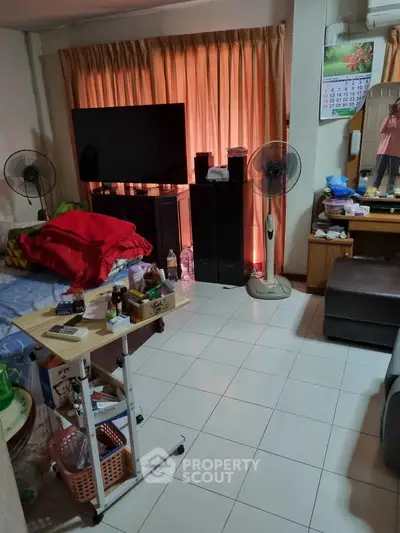 Cozy living room with tiled floor, large TV, and ample natural light from curtains.